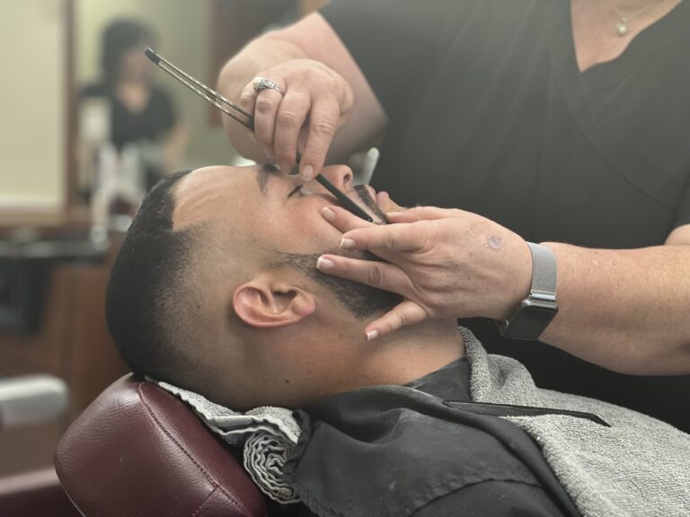 Barber trimming a man's beard with shears